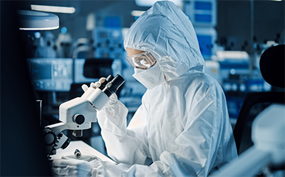 Pyrogen Testing Webpage Picture A scientist wearing full PPE observes a sample on a microscope.