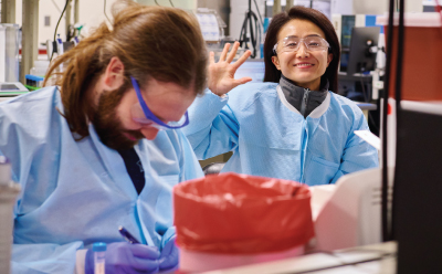 一位面带微笑的科学家在实验室与同事们一起工作。