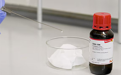 Laboratory vial with a red cap beside a small pile of white powder on a glass surface.