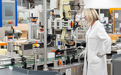 Contract Manufacturing for IVD, Medical Device, and Biologicals Woman in a labcoat and goggles inspecting a lateral flow membrane manufacturing line.