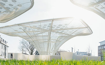 Curved white solar canopy structures A futuristic outdoor scene with curved white solar canopy structures and solar panels, set against a bright sky and surrounding greenery.
