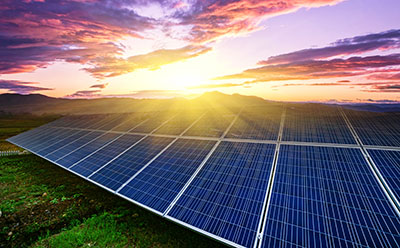 Light harvesting Ground-mounted solar panels capturing sunlight at sunrise, with colourful clouds and distant mountains in the background.