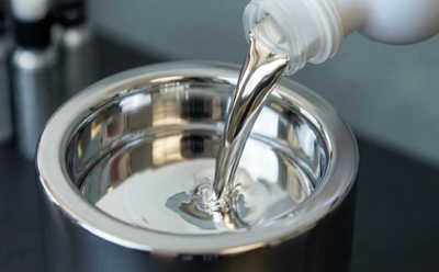 Liquid Alloy Pouring A metallic container with a reflective surface, being filled with a clear, shiny liquid alloy from a white bottle.. Image is AI generated.