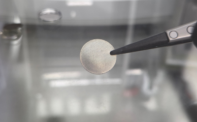 High Purity Metals in Batteries 一只镊子夹着一枚金属圆盘,背景模糊。