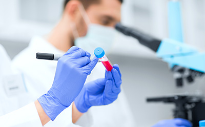 Laboratory labels 一个身穿白大褂的人站在实验室里,面向镜头,拿着剪贴板写着笔记。实验室里的架子上摆放着各种实验设备,如烧杯、烧瓶、试管和装有标有不同颜色化学试剂的瓶子。