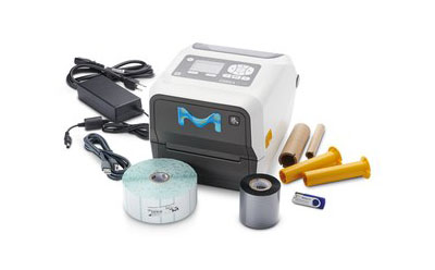 MilliSentials™ Lab Labeling System 便携式小型标签打印机,机身为白色和灰色相间,正面印有蓝色 "M "标志。与打印机配套的还有各种配件,包括一个带电缆的电源适配器、三个类似墨水卷的圆柱形物体(颜色分别为黄色和黑色)、一个蓝色塑料小部件(似乎是打印机机械装置的一部分)和一卷标签。