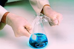一个戴着实验室手套的人正在给装有蓝色液体的烧瓶贴密封膜