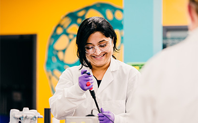 Antigen discovery Scientist smiling while using a micropipettor to pipet in the lab.