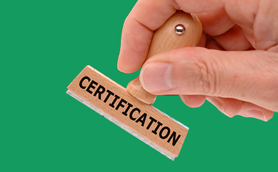 药典和计量研究院标准 画面描绘了一只手准备盖上标有 "CERTIFICATION"(认证)字样的木质橡皮图章,背景是一片生机勃勃的绿色。