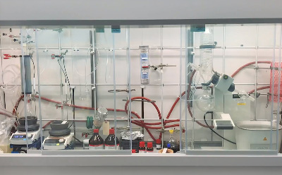 Representative Organic Reaction Toolbox Setup Featuring Common Synthesis and Workup Equipment. A laboratory fume hood displaying an organized organic synthesis workstation, including hot plates, condensers, glassware, tubing, reagent bottles, and a rotary evaporator arranged for conducting and optimizing chemical reactions.