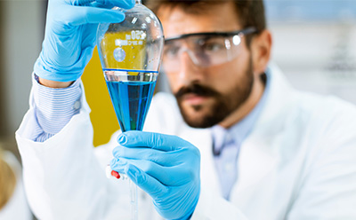 Scientist handling a separatory funnel filled with a blue solution during a laboratory workflow. A laboratory researcher wearing protective gloves carefully operates a separatory funnel containing a blue liquid, with additional lab equipment visible in the background.