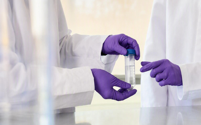 Managing Nitrite Impurities Close-up of gloved hands examining a liquid-filled sample container in a laboratory setting.