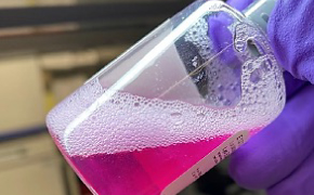 The product bottle of the rehydrated EDM gel, slanted and facing the top right corner. Fingers hold the bottle top.