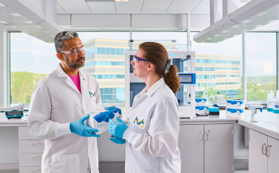 Two scientists talking with the AAW™ liquid handling workstation in the background.