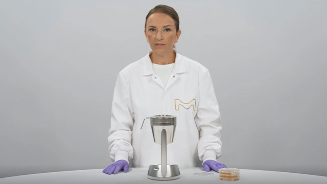<p>MAS-100 Sirius<sup>®</sup> Microbial Air Sampler</p>
Scientist in a white lab coat and purple gloves standing at a laboratory bench