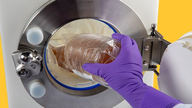 <p>确保洁净室合规性以实现安全物料转移</p> A close-up image of a gloved hand placing a sealed petri dish into a circular opening of a laboratory device. The device features a metal rim and a bright blue background, emphasizing a sterile and controlled environment for scientific work.