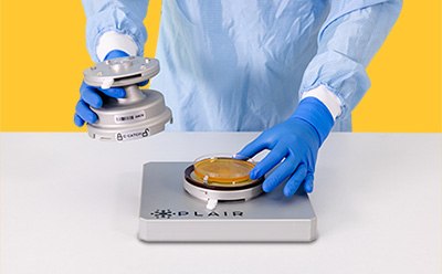 A technician in protective gear carefully handles a C-Catch unit while placing a petri dish on the monitoring platform. 