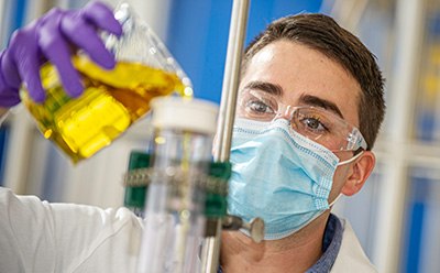 Worker in QC lab pouring liquid from a beaker into a tube, representing {hcompnay}'s quality control (QC) workflow products for medical device manufacturing.