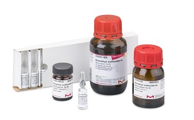 A collection of NMR solvents displayed on a white surface, including two large brown bottles with red caps, a small vial, and a set of glass ampoules in a white box, all labeled for precise spectroscopic analysis.