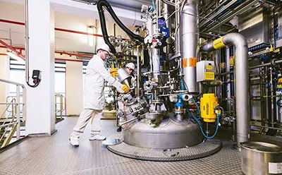 Two technicians working on large, two-story vessel for catalyst production