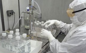 在生物工艺实验室中，身着洁净室防护服的技术员正在处理细胞培养液，背景是整齐排列的密封培养基瓶，表示生物工艺的无菌受控环境。