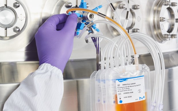 Hands of a person in a labcoat and gloves working with a sampling system attached to a stainless steel bioreactor.