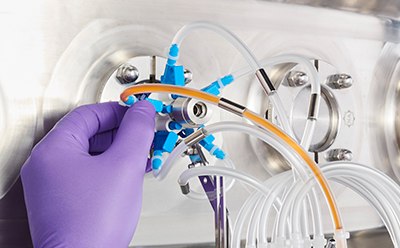 一个戴着紫色手套的人正在调整连接到金属医疗设备上的透明塑料管。该装置有多个出口，管子汇合处有一个蓝色接点。
