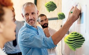 Group of people near a white board, one man is writing on the board. 