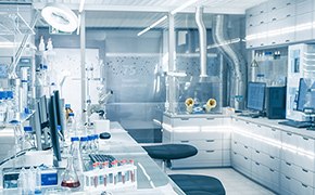 Lab with white cupboards and chemistry lab equipment used for quantitative analysis is shown without any people working. Fume hood, glass vials and beakers are visible.