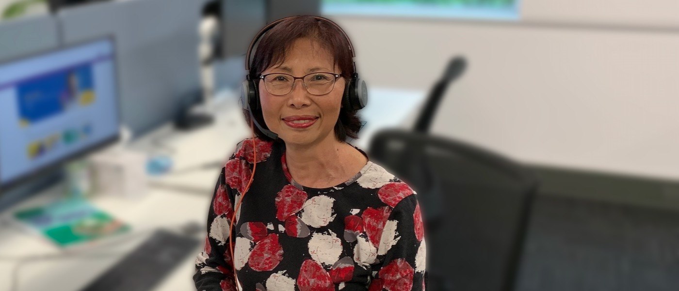 Grace Yee wears a headset and sits at her desk. In the background is her desktop computer. 