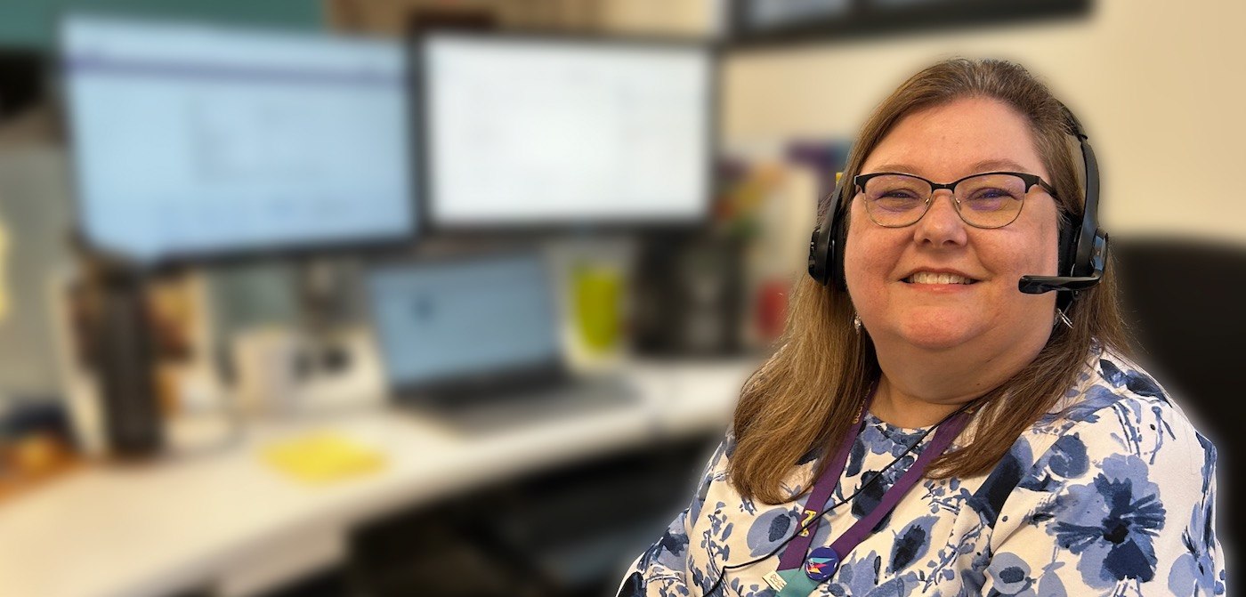 Paul Shively sits at her desk wearing a headset. Behind her her desktop screens are blurred