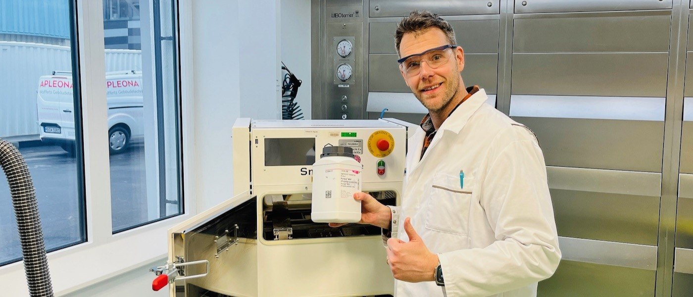 Thomas Kipping wears safety glasses and a lab coat standing next to a laser 3D printer.