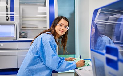 Female scientist in a blue lab coat completing paperwork on the lab bench of the molecular contract testing laboratory. 