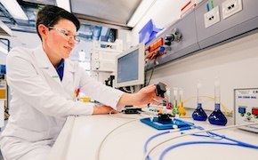 Scientist in a lab, in front of a monitor, using some test tubes to run experiments