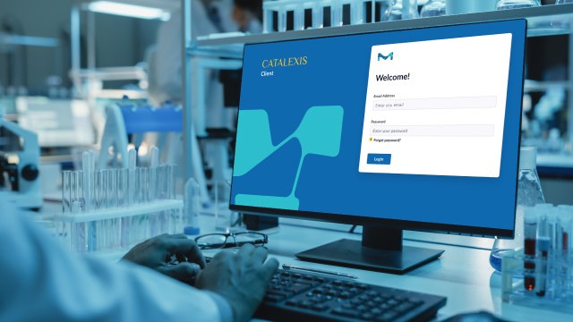 Chemist, who is not visible, views the logon screen for Catalexis in a well-equipped chemistry lab with advanced instruments.