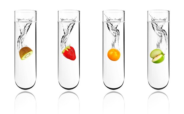 Four test tubes contain water and various fruits – kiwi, strawberry, orange, and green apple – with splashes inside, representing natural flavors for assessment.