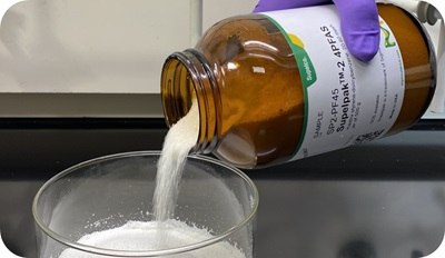 Amber reagent bottle labeled Supelpak 2 PFAS adsorbent pouring purified XAD-2 resin granules into a glass beaker for PFAS air emissions analysis.